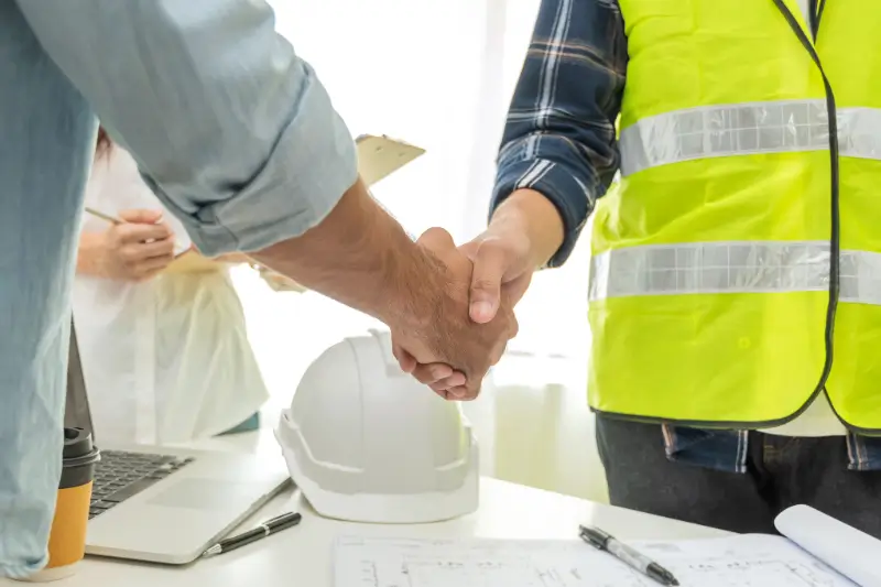 Two people in safety vests shaking hands at a desk